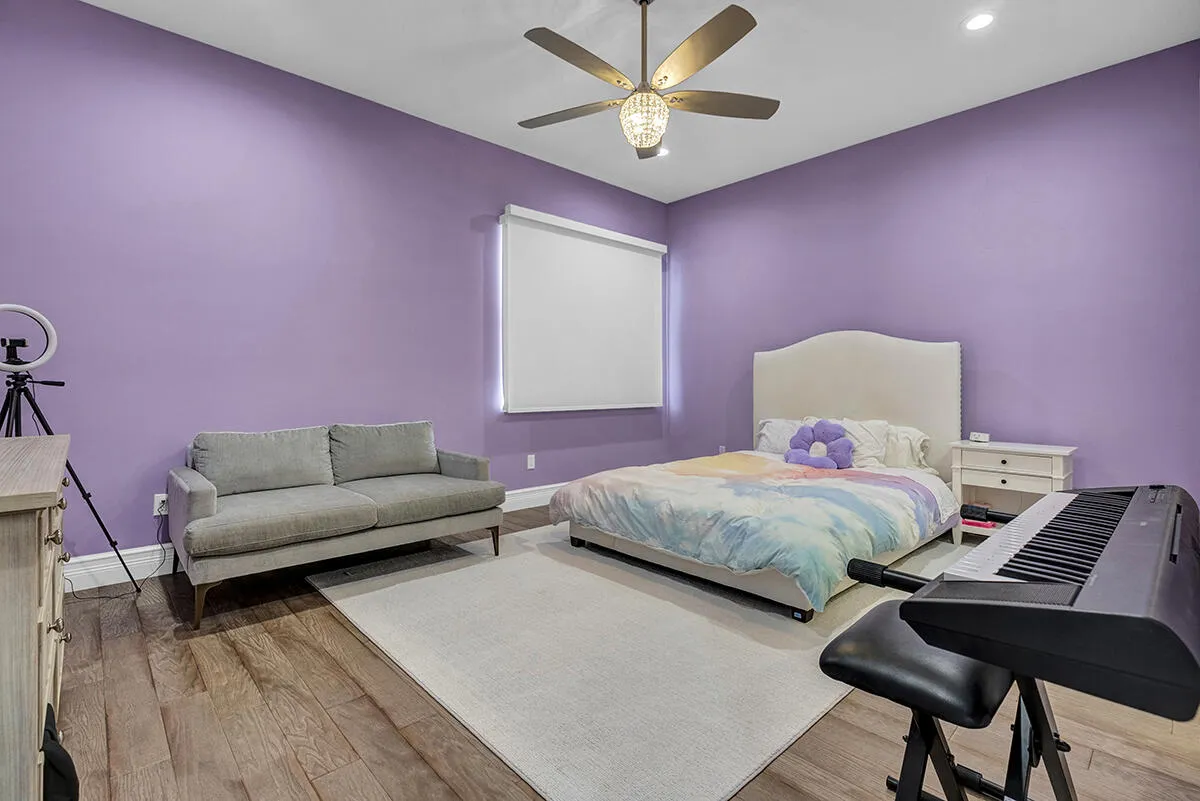 Spacious room featuring wood-finish flooring, purple painted walls, and a large window with a roller shade