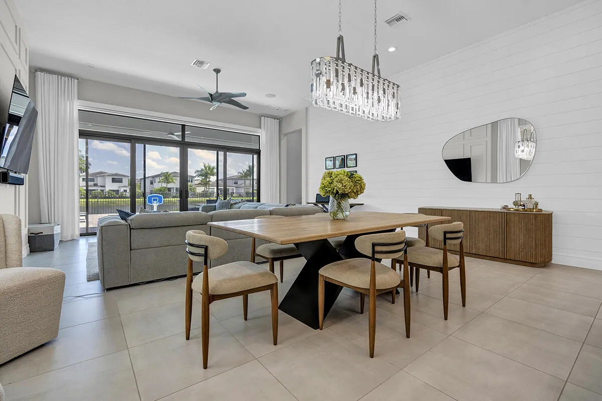 Open-concept dining and living area featuring large format tile flooring, a linear crystal chandelier, and a shiplap accent wall