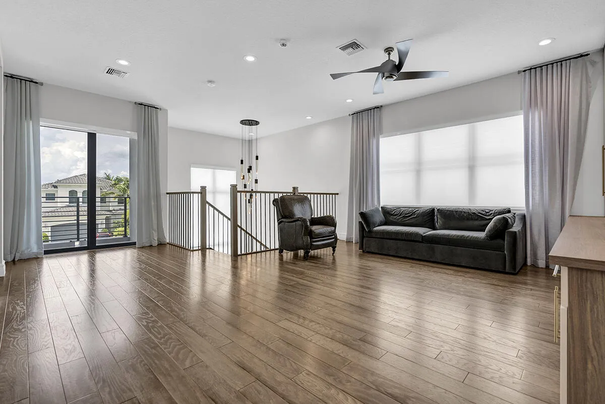 Spacious room featuring wood-finish flooring, a large sliding glass door with a balcony, and a prominent multi-blade ceiling fan