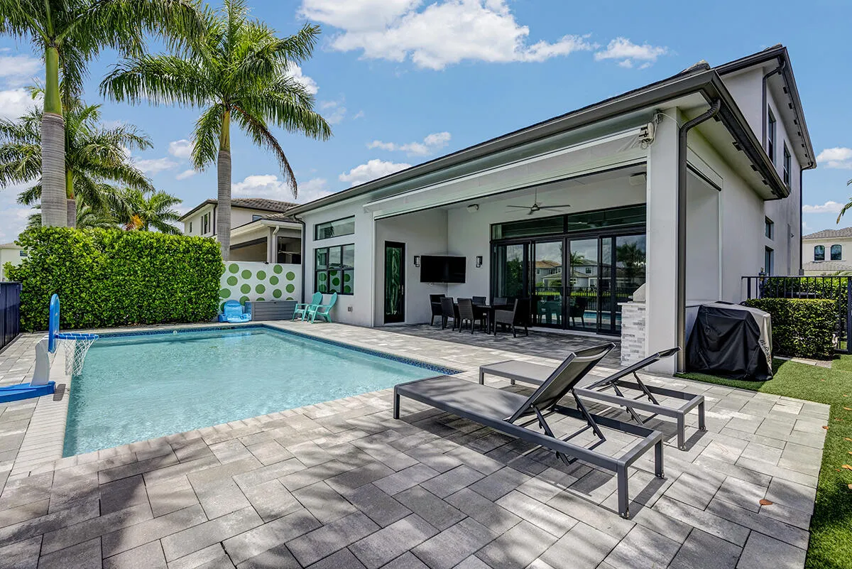 Outdoor living area featuring a rectangular pool with paver decking, an expansive covered patio, large sliding glass doors, and mature palm trees