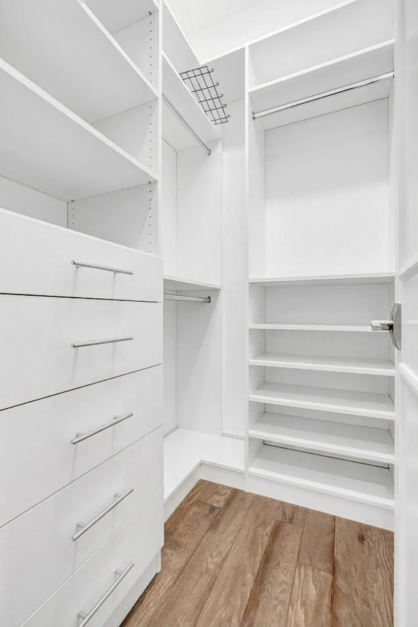 Custom closet system featuring multiple hanging rods, built-in shelving, integrated drawers with brushed nickel pulls, a wire storage rack, and wood-finish flooring