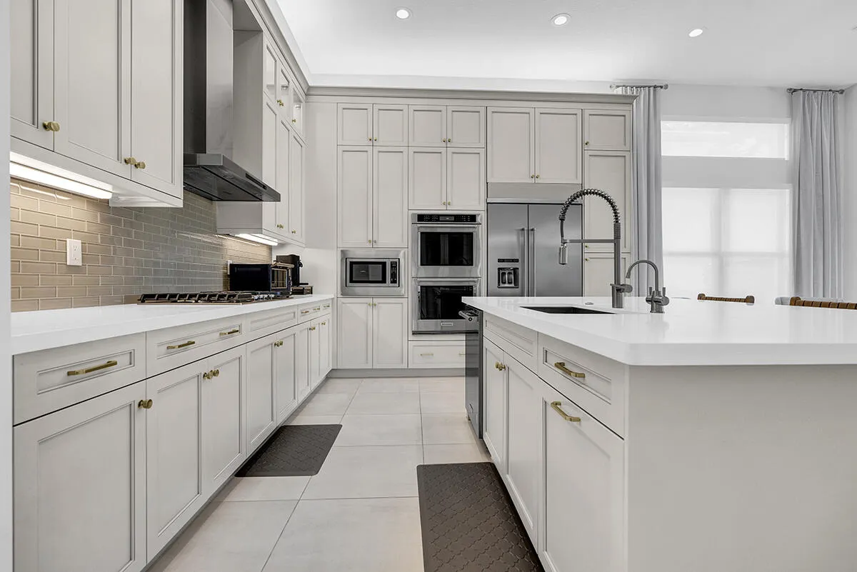 Gourmet kitchen featuring extensive light cabinetry, light countertops, a large center island with an undermount sink, stainless steel appliances, and a subway tile backsplash