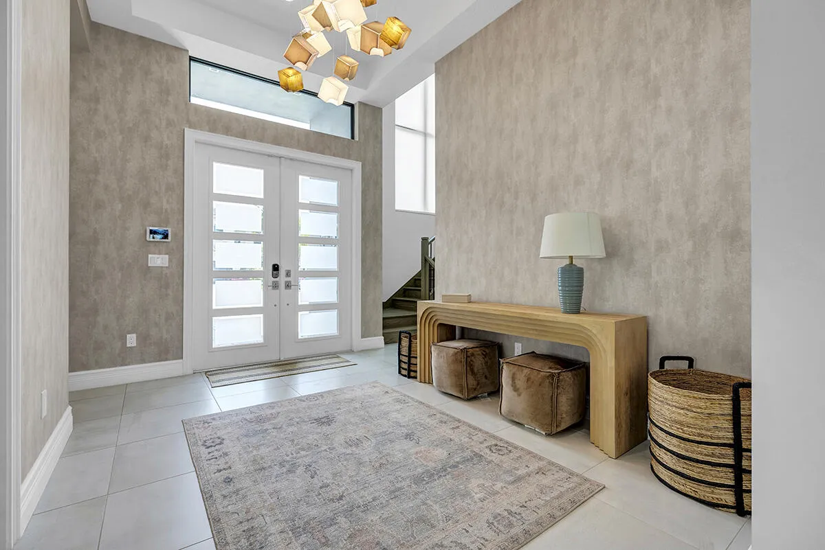 Grand entry foyer featuring double frosted-pane doors with transom window, light-toned textured wall treatment, and light-colored tile flooring
