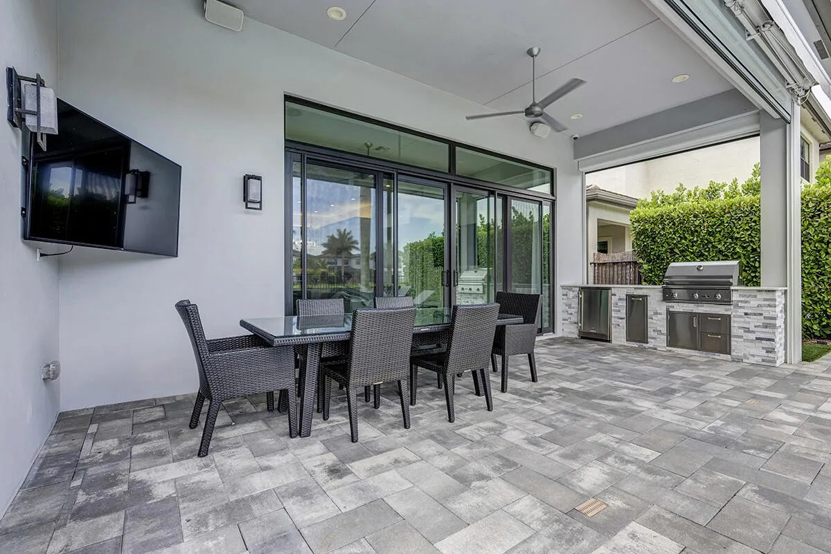 Expansive outdoor patio featuring gray paver flooring and an integrated outdoor kitchen with stainless steel appliances and stone veneer detailing