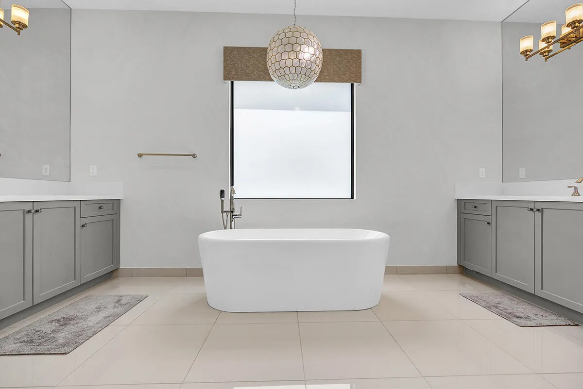 Freestanding soaking tub with a floor-mounted faucet, flanked by dual vanities with gray cabinetry and white countertops