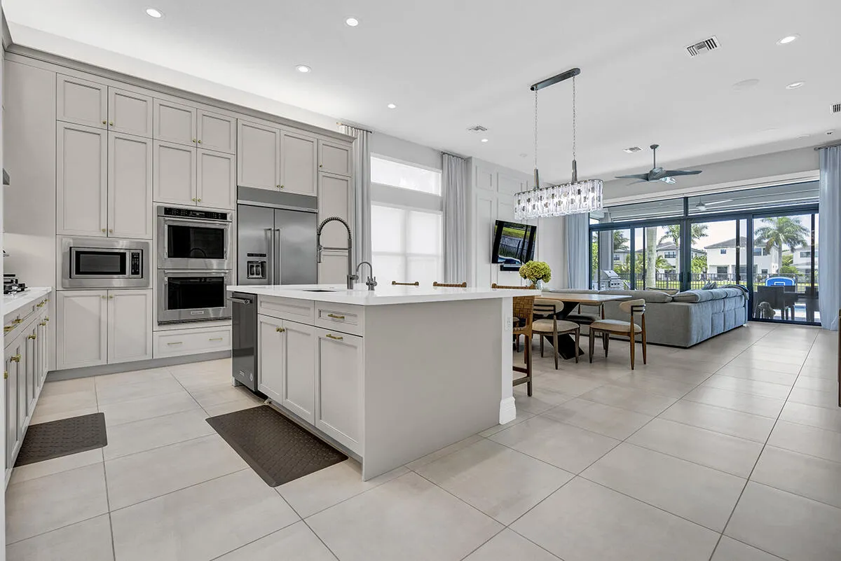 Contemporary kitchen featuring extensive cabinetry, stainless steel appliances, a center island with sink, and large format tile flooring