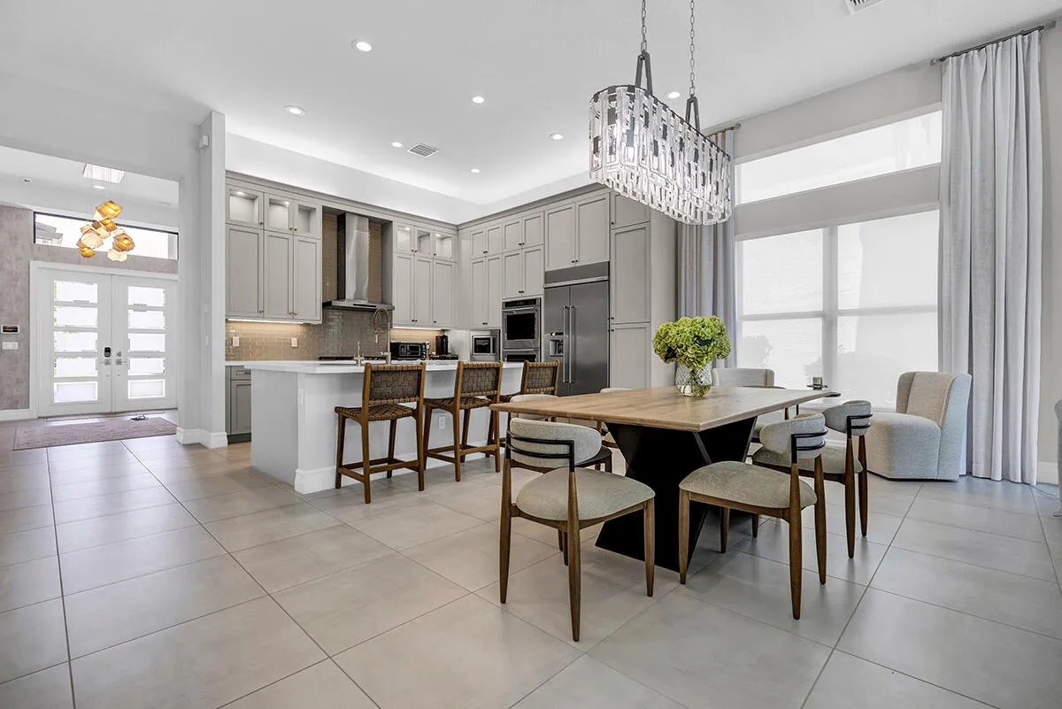 Spacious open-concept living area featuring large format tile flooring, a gourmet kitchen with extensive cabinetry, a central island with bar seating, and integrated stainless steel appliances