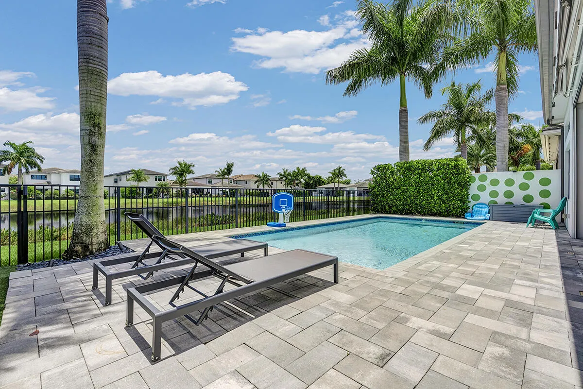 Private swimming pool with paver patio, surrounded by lush landscaping and a black wrought-iron fence