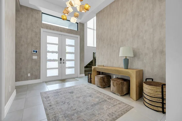 Grand entry foyer featuring double frosted-pane doors with transom window, light-toned textured wall treatment, and light-colored tile flooring