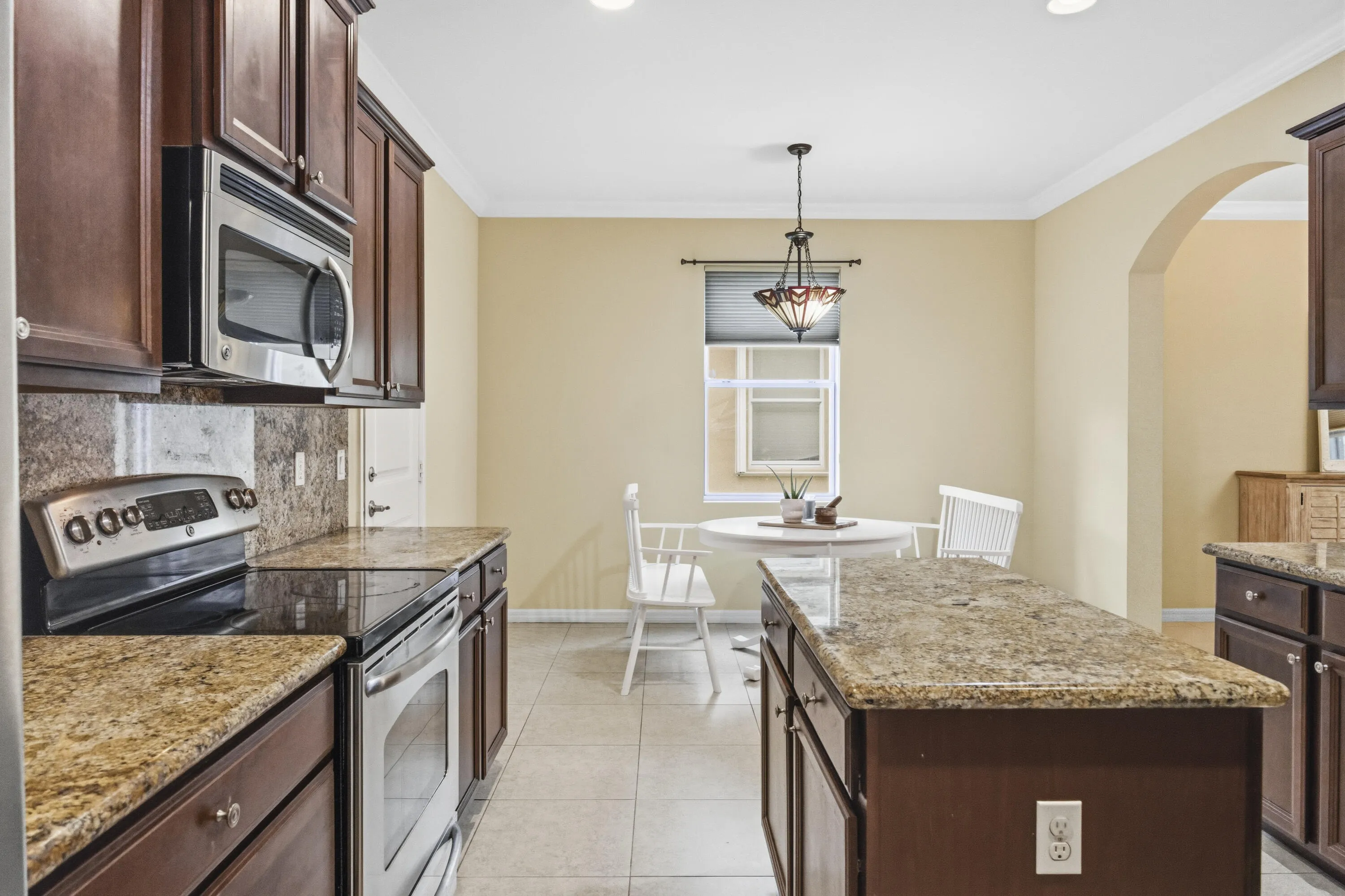 Stainless steel appliances, built-in microwave, wood cabinetry, stone countertops, and tile flooring