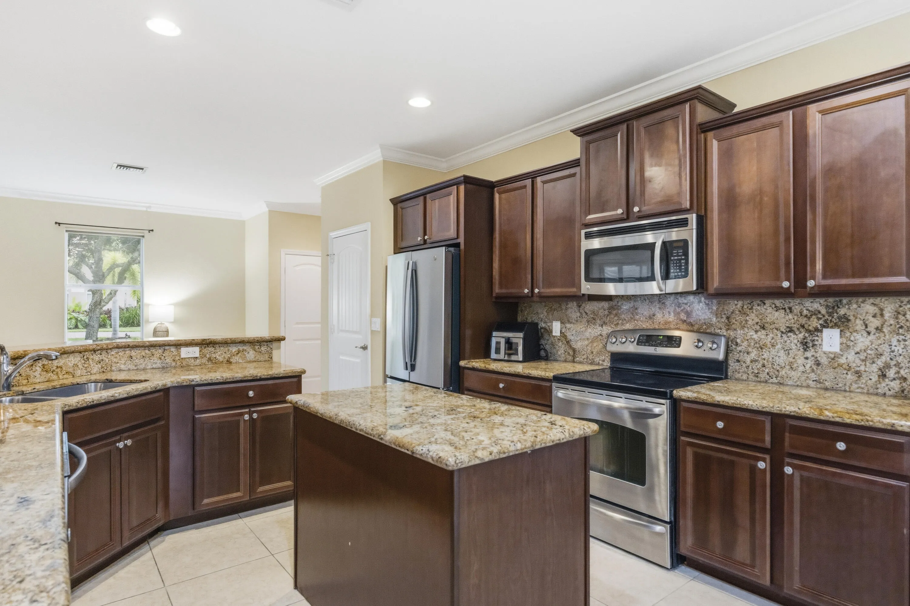 Kitchen featuring wood cabinetry, stainless steel appliances, granite countertops, a center island, and tile flooring