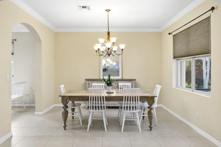 Recessed window with privacy blinds, archway entry, tiled flooring, crown molding, and a chandelier with frosted glass shades