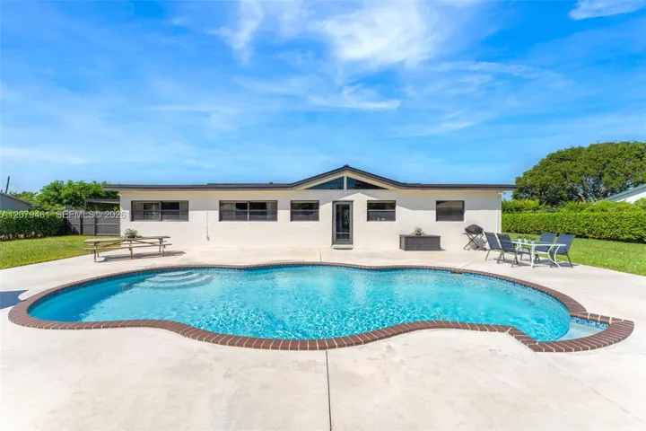 Rear exterior featuring a stucco facade with a gable roofline, concrete patio, and in-ground swimming pool with brick coping