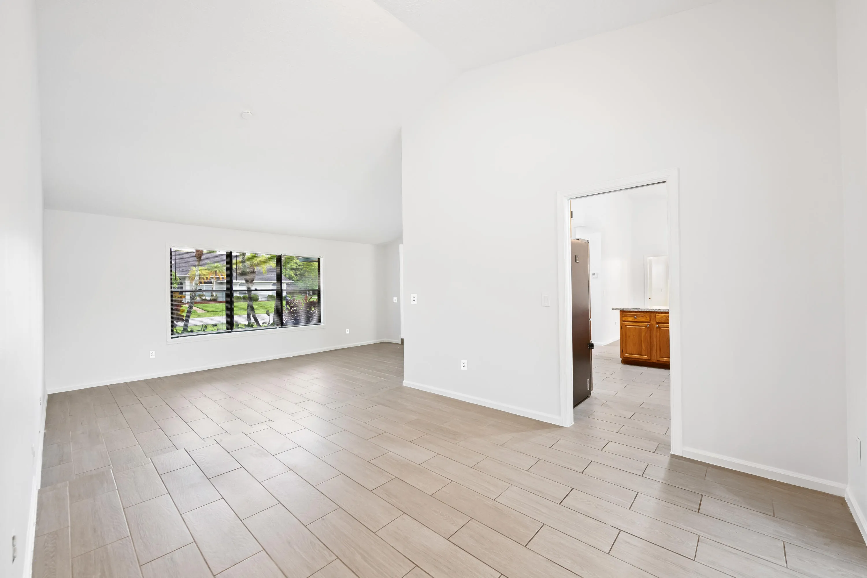 Vaulted ceilings, large window, wood-look tile flooring, and a bright, neutral color palette