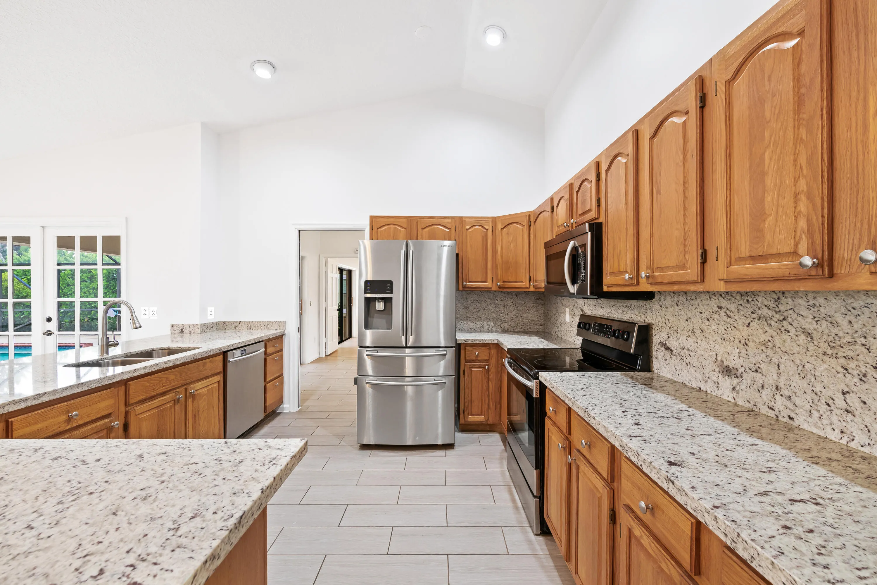Vaulted ceiling, wood cabinets, stone countertops, stainless steel appliances, and large-format tile flooring