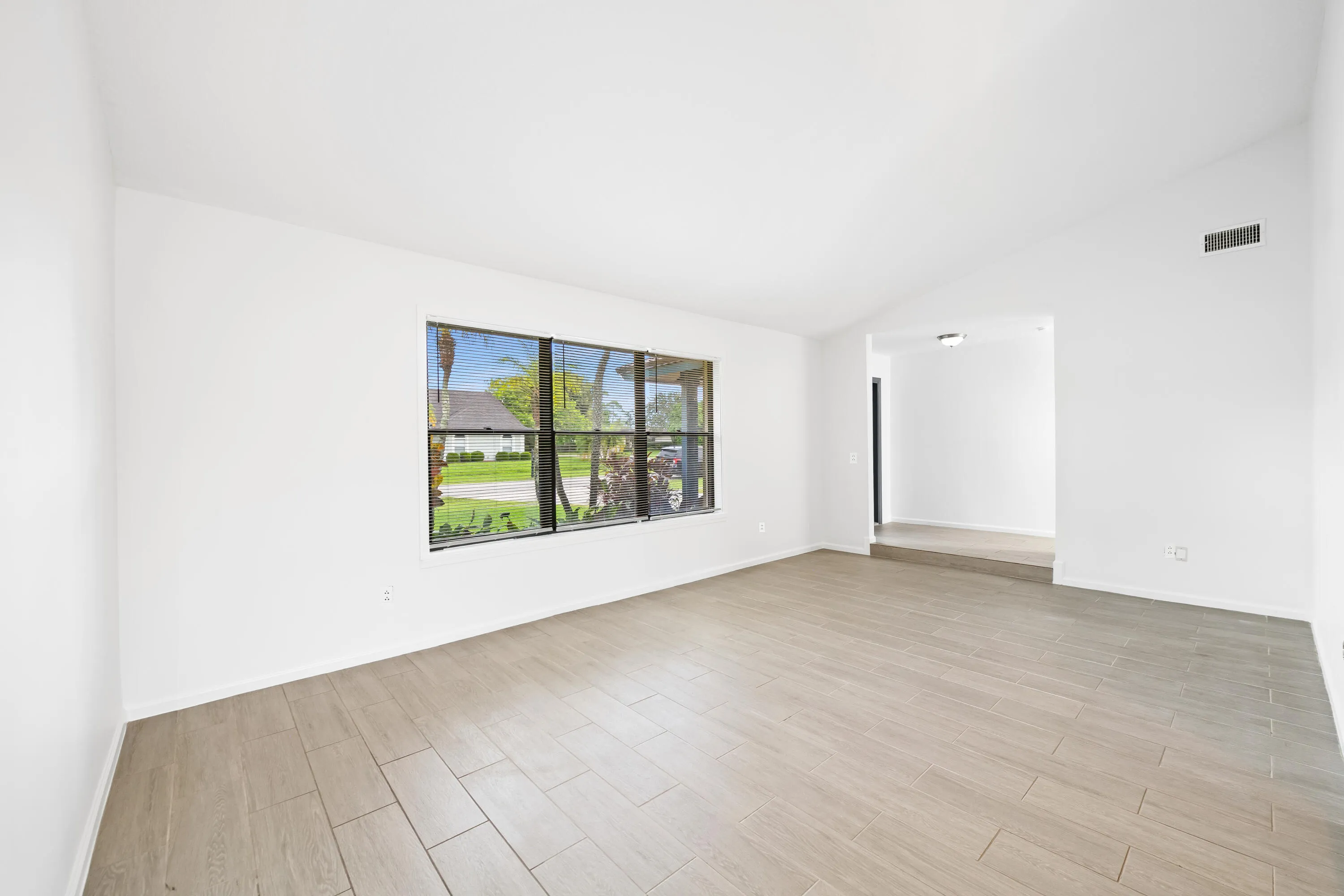 Vaulted ceiling, large window with blinds, wood-finish tile flooring, recessed entryway