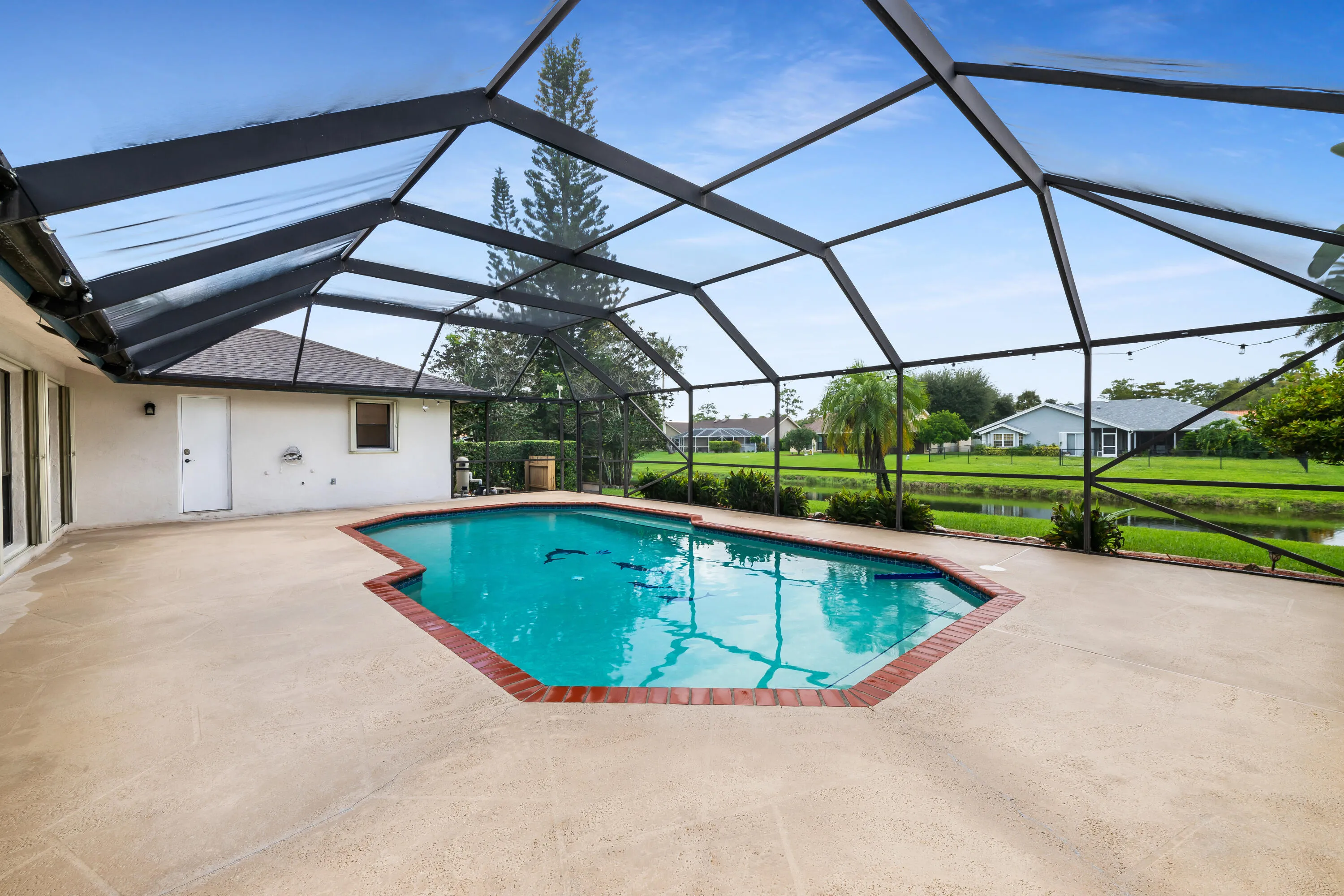 Screened-in pool area featuring a freeform pool with brick coping, expansive concrete patio, and direct access to the interior via sliding glass doors