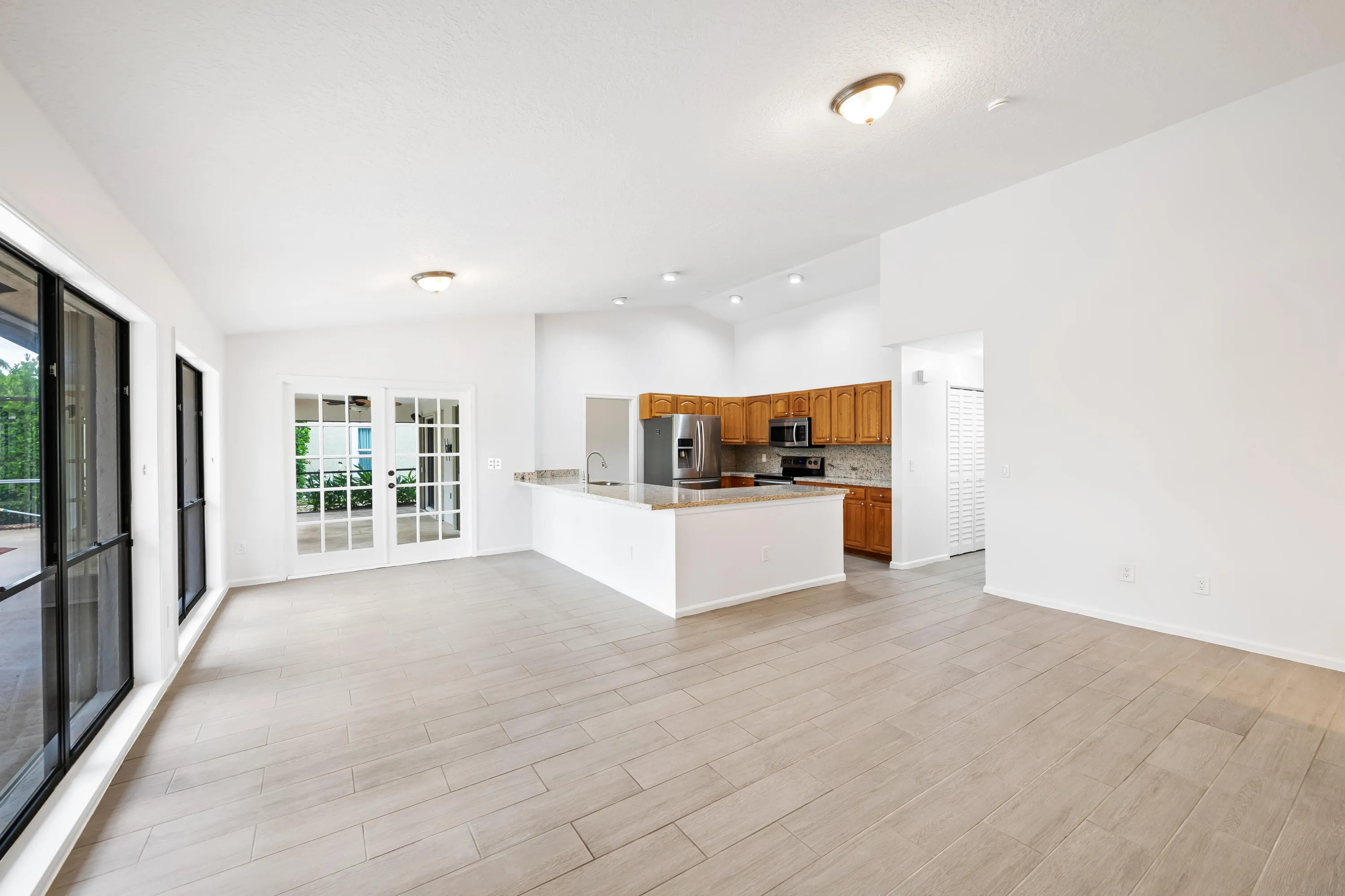Light wood-finish flooring with an open kitchen layout featuring wood cabinetry, stainless steel appliances, and a breakfast bar