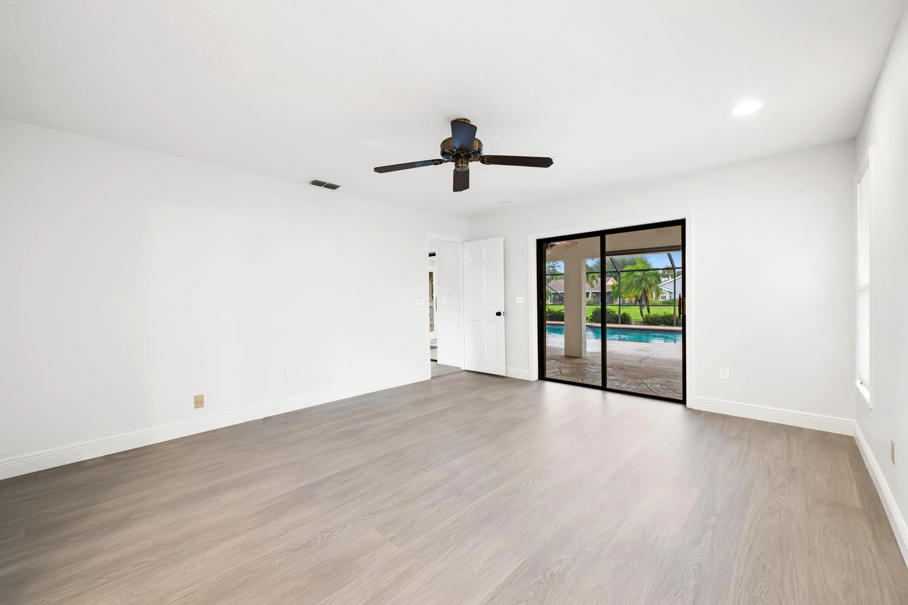 Light wood-finish flooring, white walls, black ceiling fan, recessed lighting, and black-framed sliding glass doors