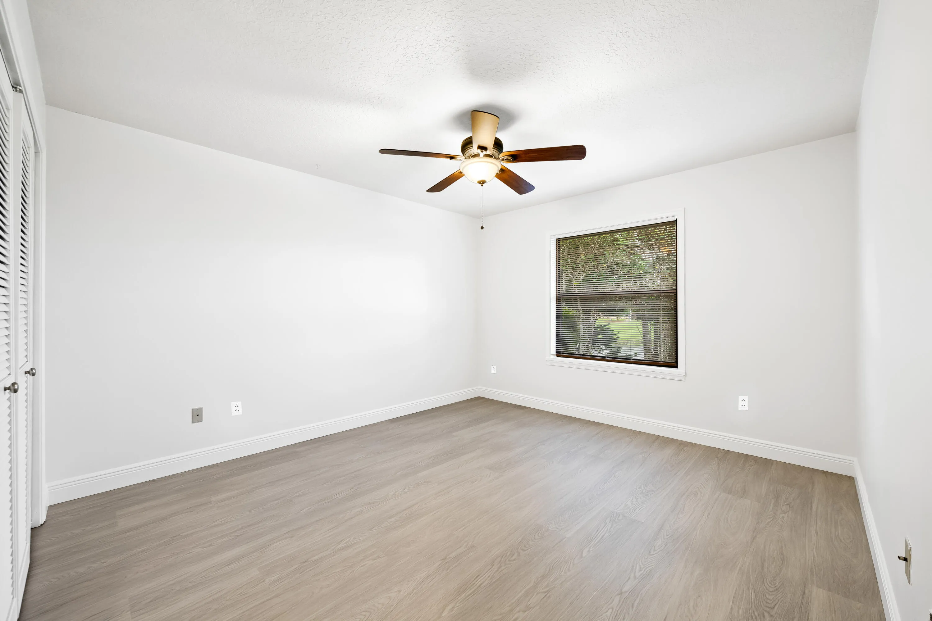 Spacious room featuring wood-finish flooring, a ceiling fan, and a window with blinds