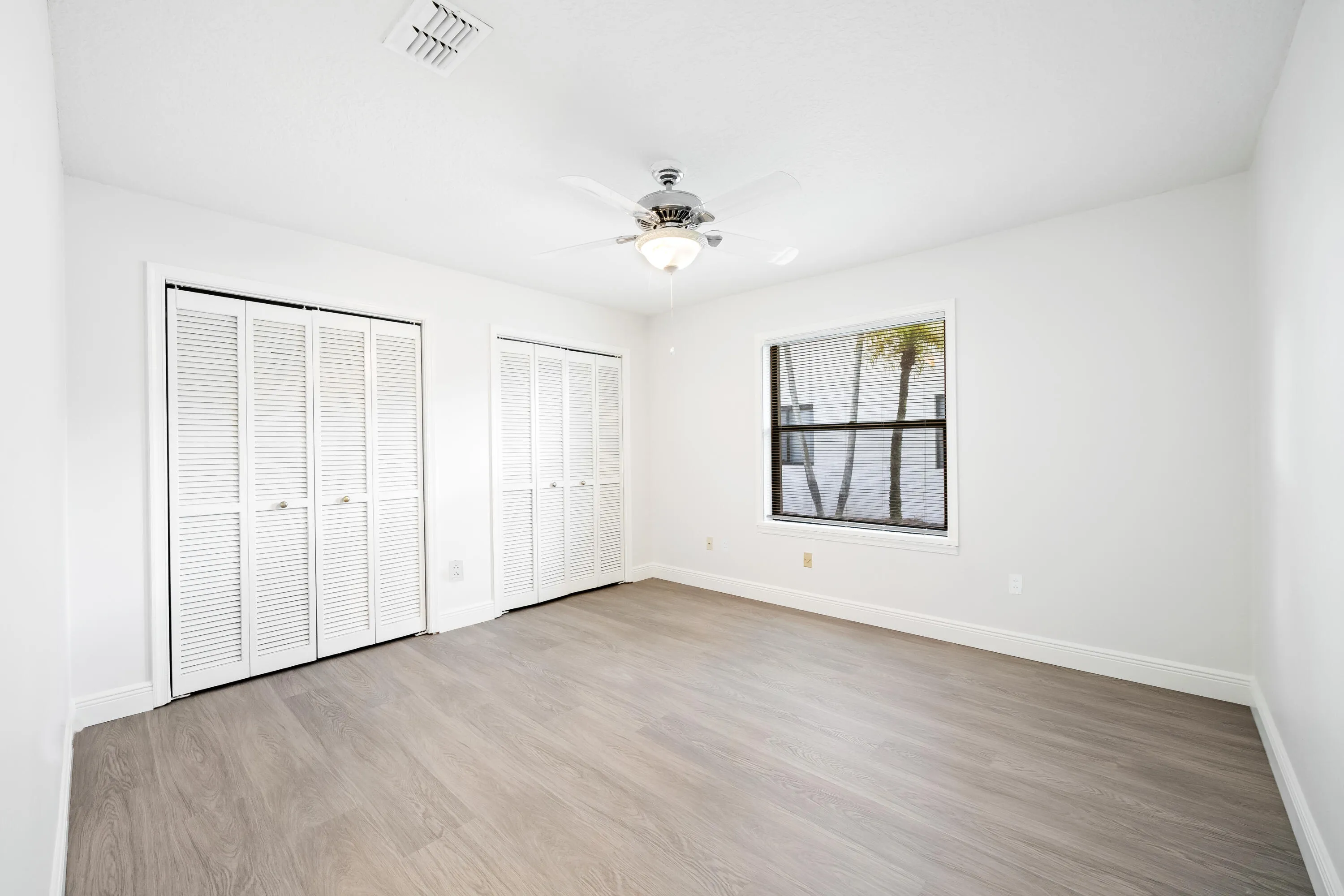 Wood-finish flooring, white walls, louvered bi-fold closet doors, ceiling fan with integrated lighting, and a window with blinds