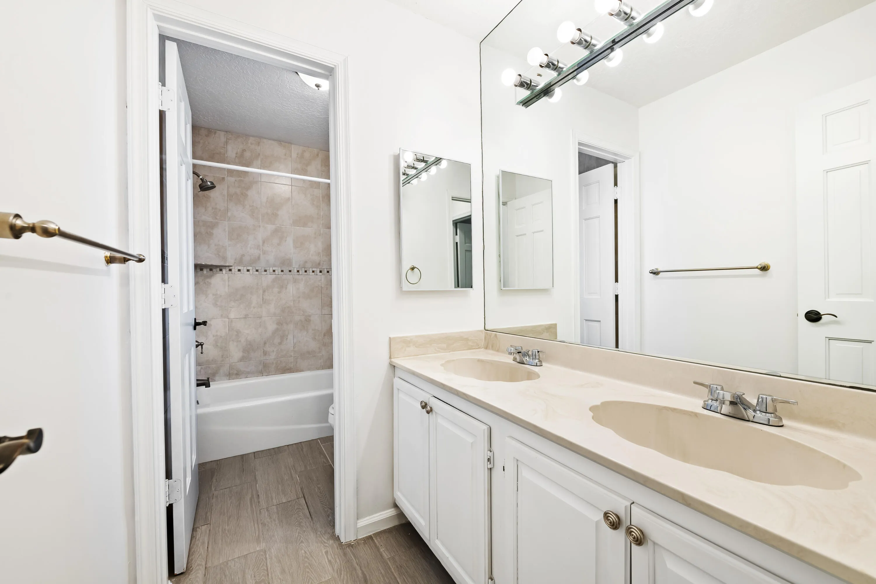Double vanity with integrated sinks and white cabinetry, large wall-mounted mirror, and tile flooring