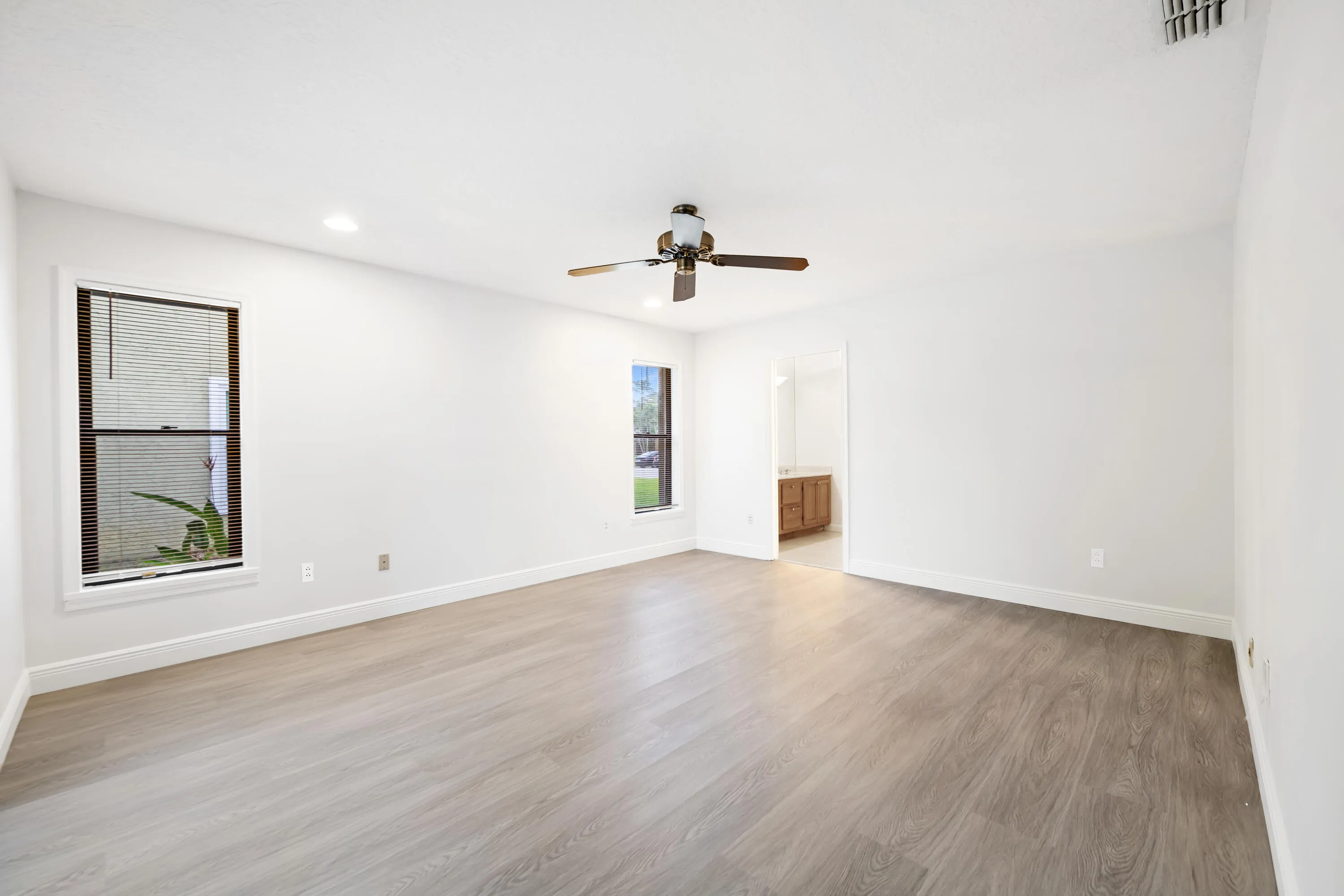 Expansive room featuring wood-finish flooring, recessed lighting, ceiling fan, and two windows