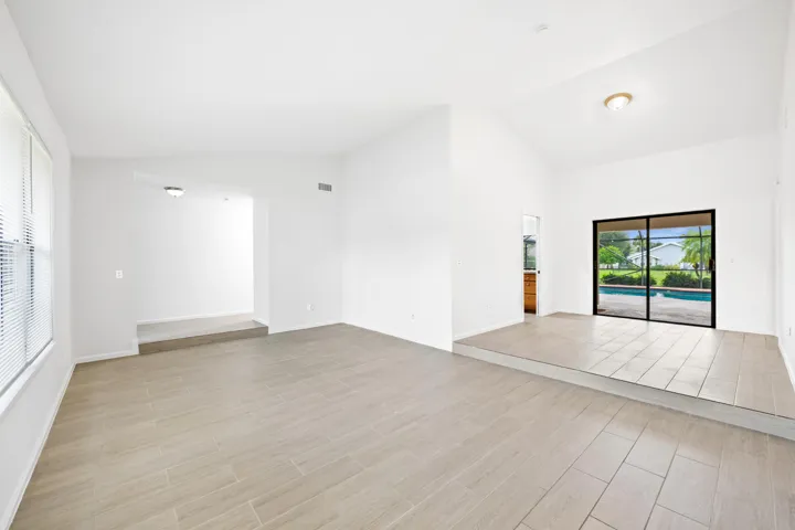 Vaulted ceiling, tile flooring, sliding glass doors, built-in recessed lighting, and a window with blinds