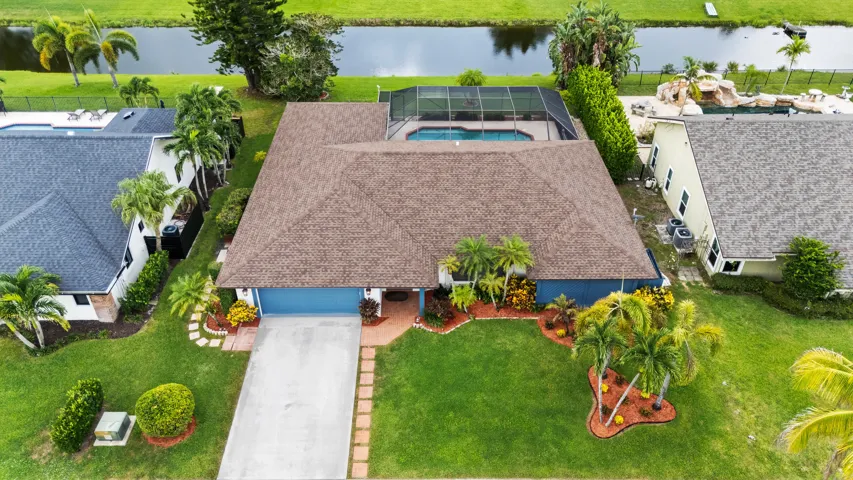 Blue exterior, brown shingle roof, screened pool enclosure, paved driveway, mature landscaping