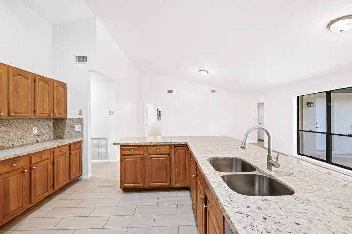 Kitchen featuring wood cabinetry, light-toned countertops, a dual-basin stainless steel sink with a gooseneck faucet, and tile flooring