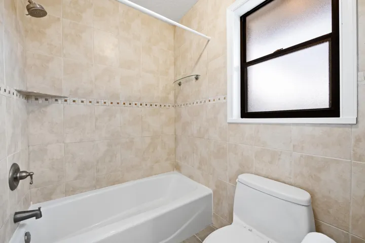 Bathtub with tiled surround and decorative accent band, bronze-finish fixtures, and a privacy window