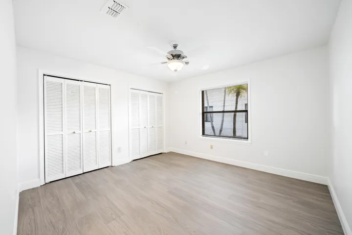 Wood-finish flooring, white walls, louvered bi-fold closet doors, ceiling fan with integrated lighting, and a window with blinds