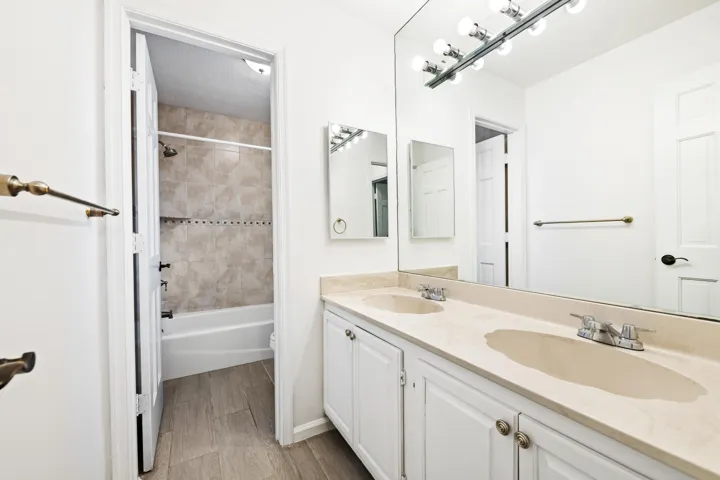 Double vanity with integrated sinks and white cabinetry, large wall-mounted mirror, and tile flooring