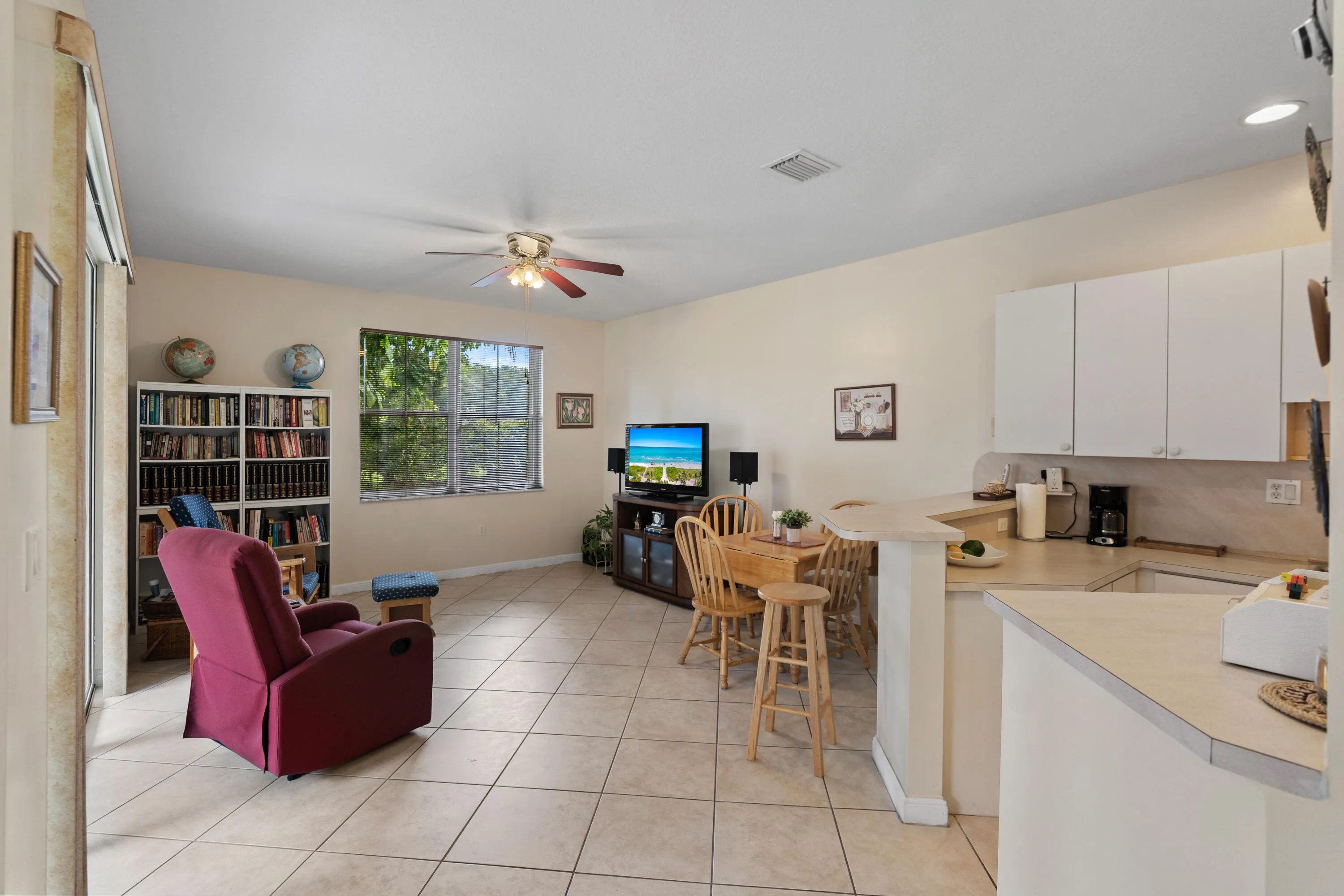 Open concept living area featuring tile flooring, ceiling fan, and a kitchen with white cabinetry and a breakfast bar
