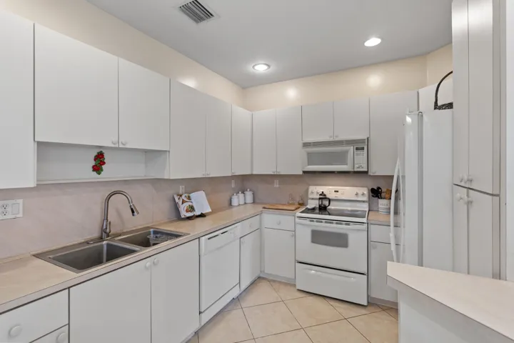 Kitchen featuring white cabinetry, a double basin stainless steel sink, tile flooring, white appliances, and recessed lighting