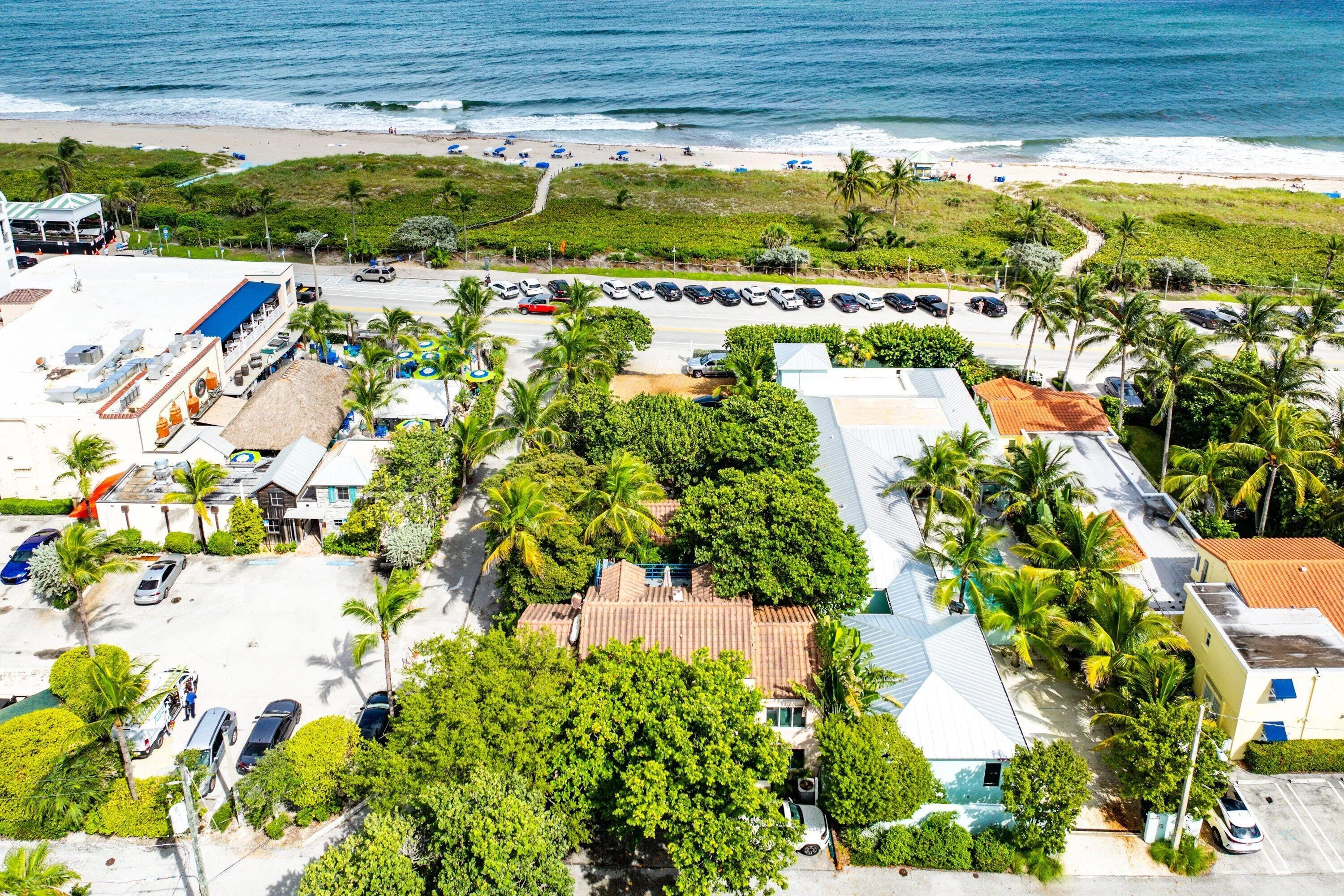 Coastal proximity, lush tropical landscaping, multiple building structures, paved parking areas, and mature palm trees