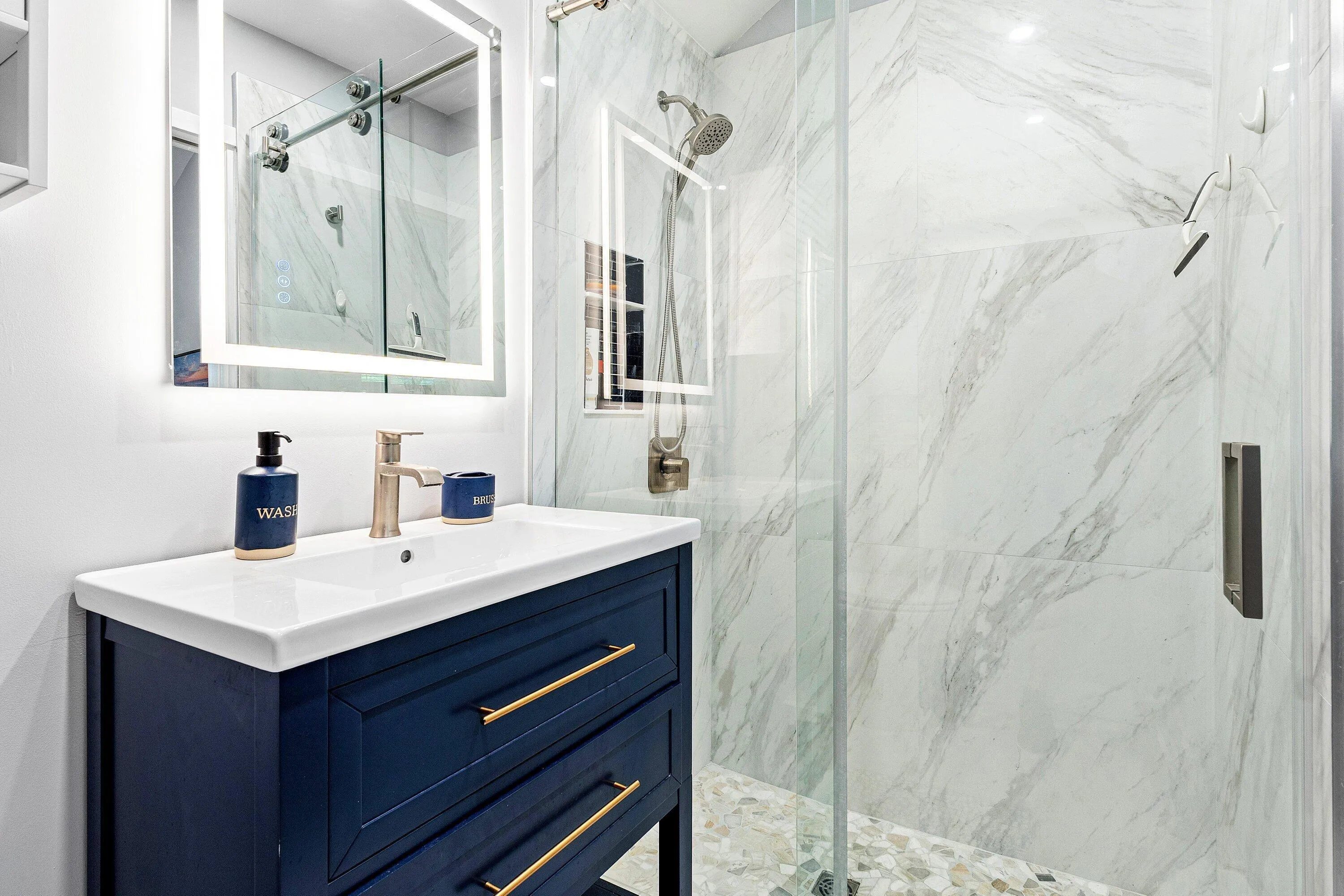 Vanity with a white ceramic basin, brass-finish faucet, and a lighted mirror