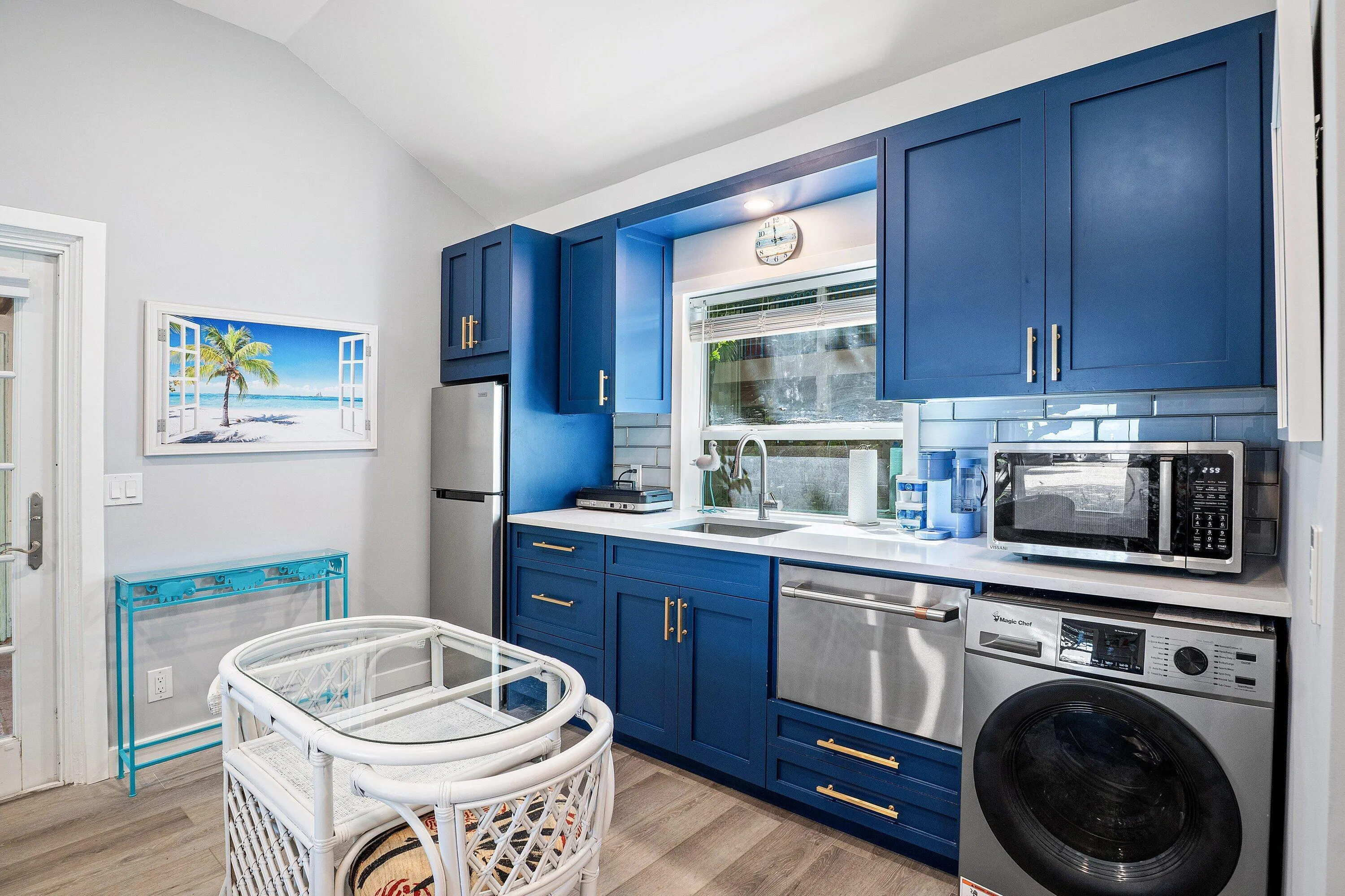 Vibrant blue cabinetry with brushed nickel hardware, light-toned countertops, a stainless steel dishwasher, a single basin sink with a chrome faucet, and wood-finish flooring