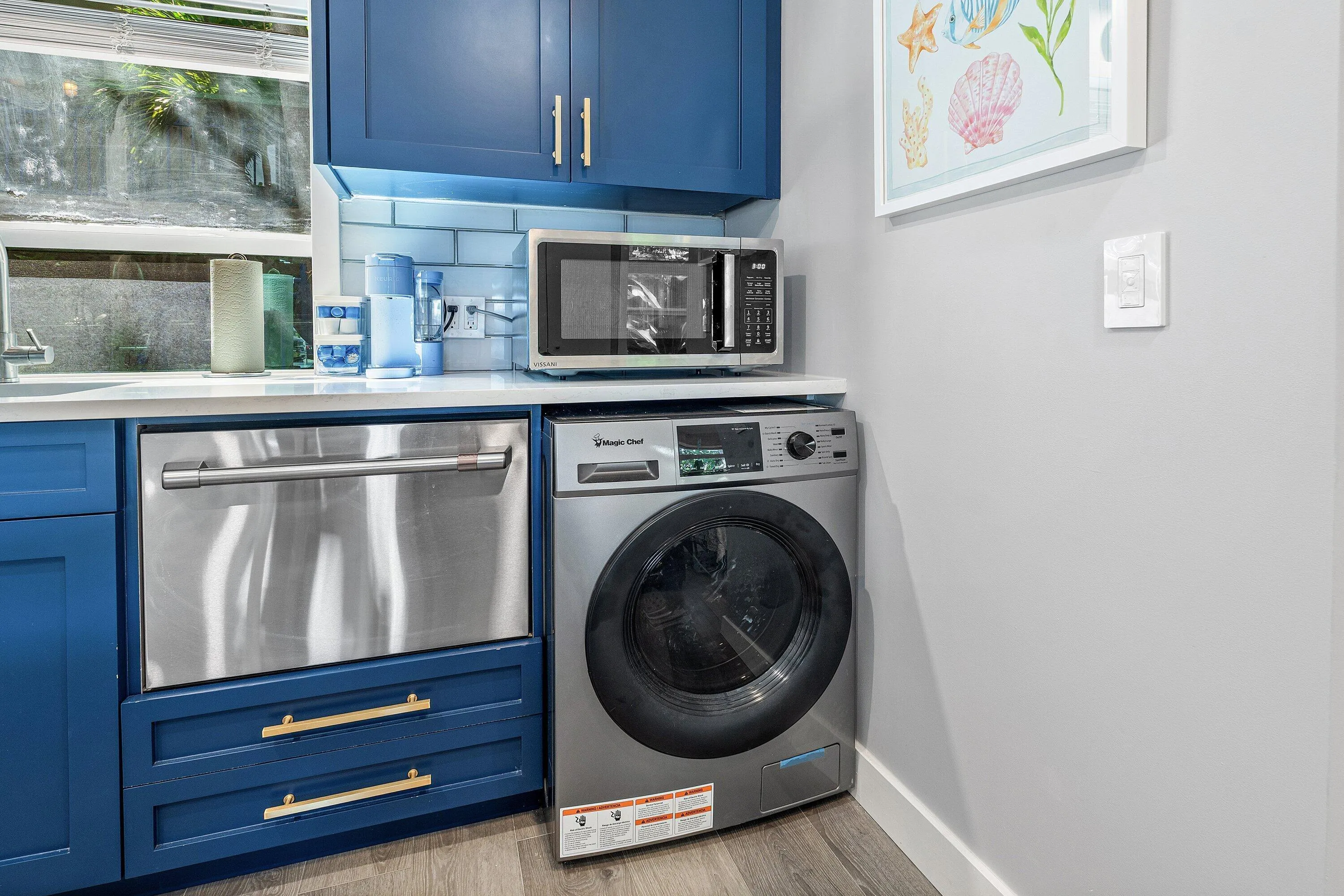Blue cabinetry with gold-tone hardware, stainless steel dishwasher, white subway tile backsplash, and light wood-finish flooring