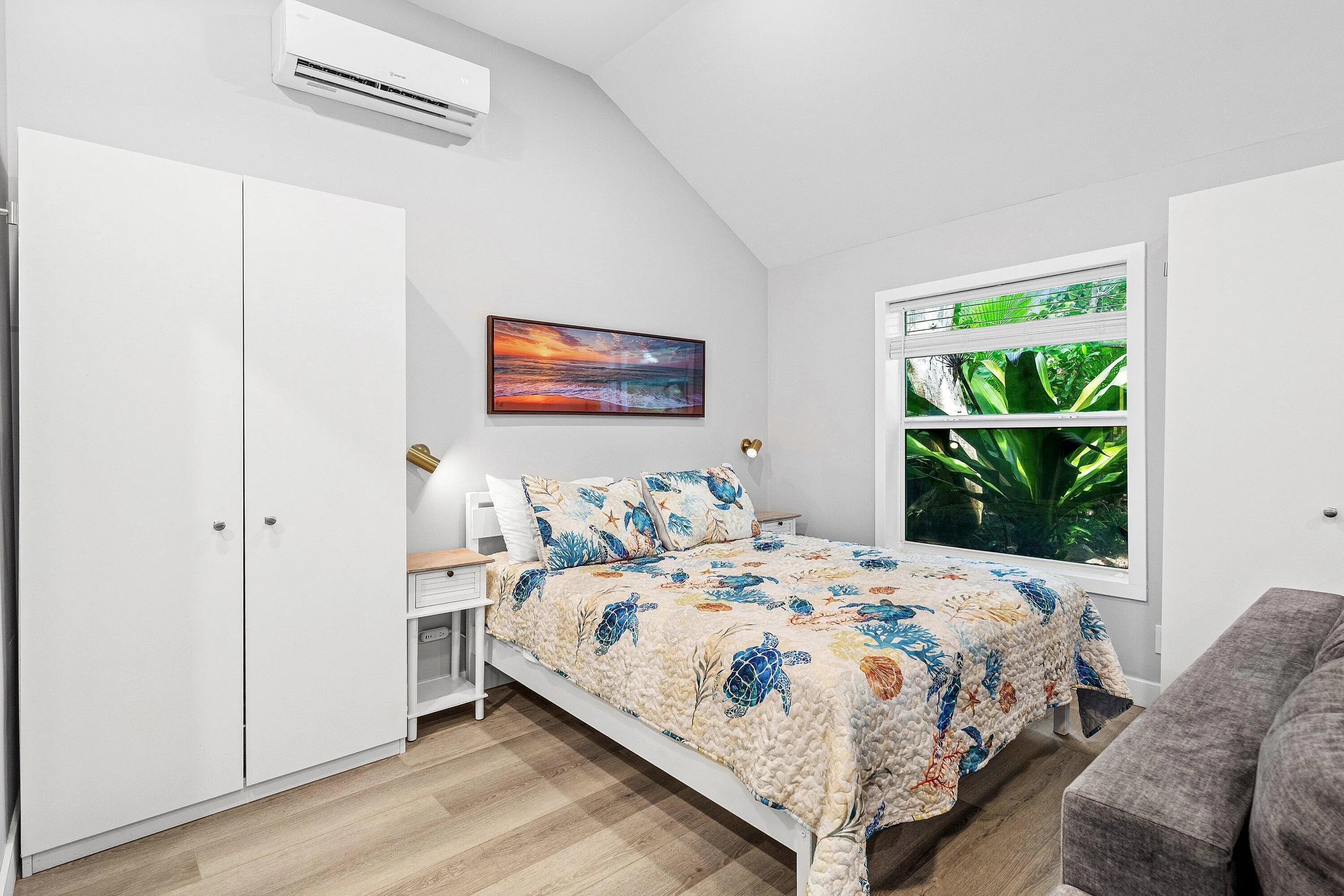 Vaulted ceiling with a wall-mounted air conditioning unit, light wood-finish flooring, and a large window