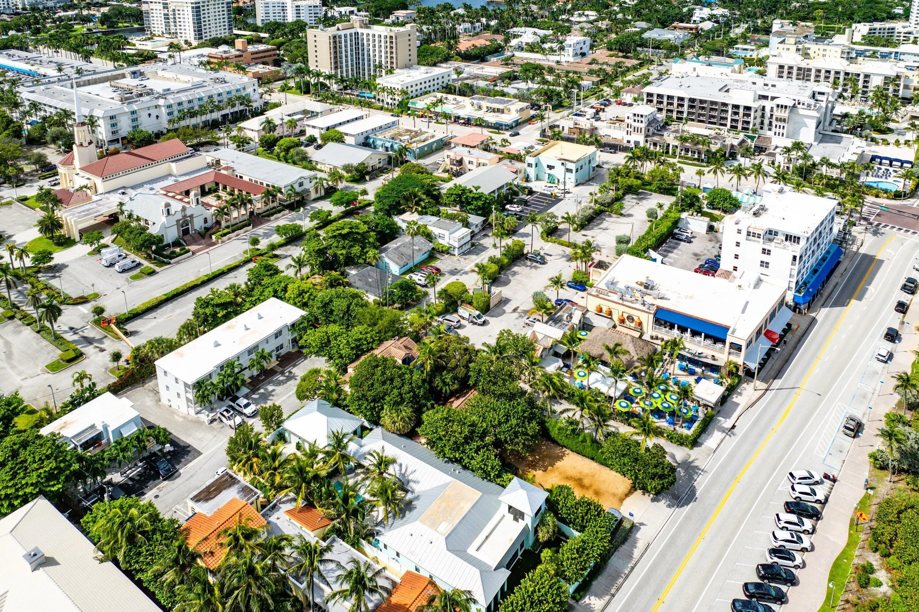 Aerial perspective showcasing a vibrant urban setting with diverse architecture, numerous commercial establishments, ample parking areas, and mature landscaping
