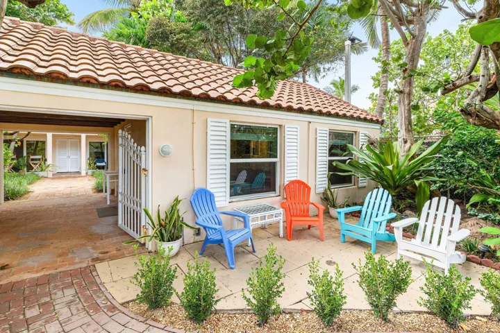 Terracotta tile roof, stucco exterior, decorative window shutters, paved patio area, and lush landscaping