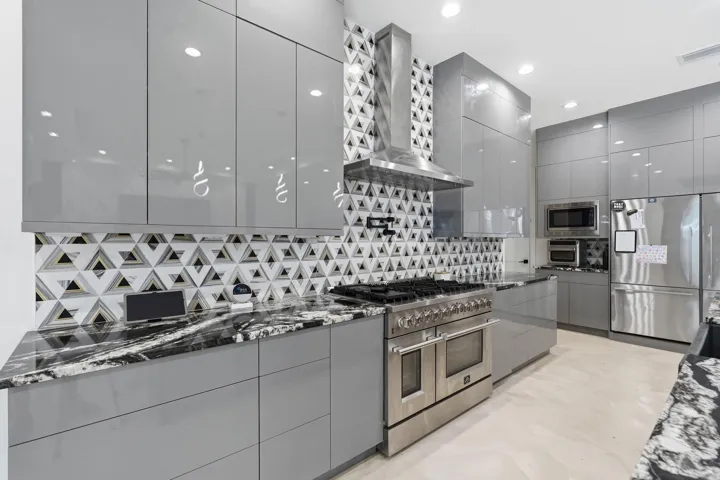Glossy gray cabinetry paired with a striking geometric tile backsplash, stainless steel appliances, and dark marbled countertops