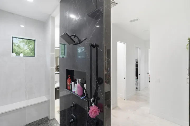 Spacious shower enclosure with dark stone-finish accent wall, built-in niche, and matte black shower fixtures