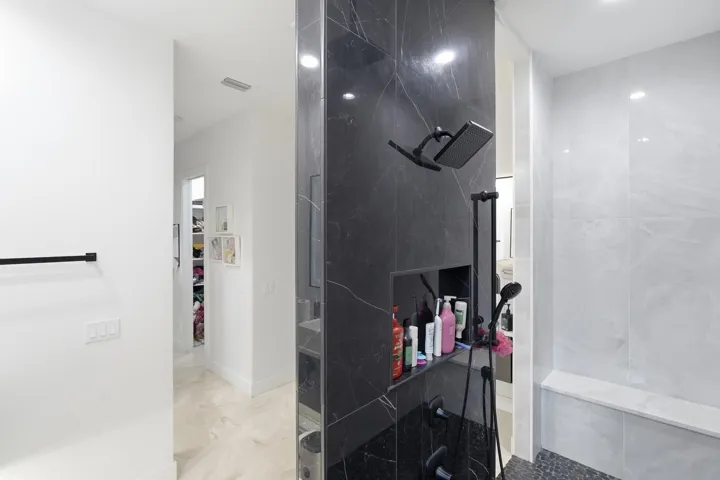 Shower featuring black marble-finish tile, a rainfall showerhead, a built-in shower niche, and a shower bench