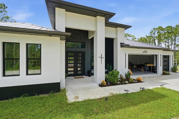 Contemporary stucco exterior with a metal roof, prominent architectural columns, a two-car garage, and a modern glass-paneled entry door