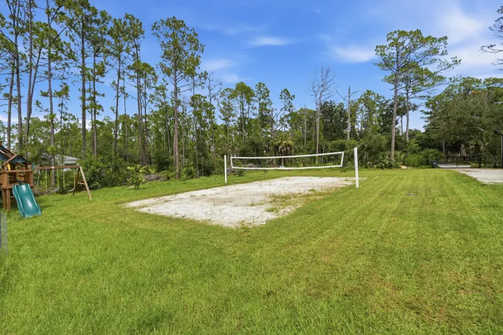 Expansive lawn featuring a sand volleyball court and a wooden playset