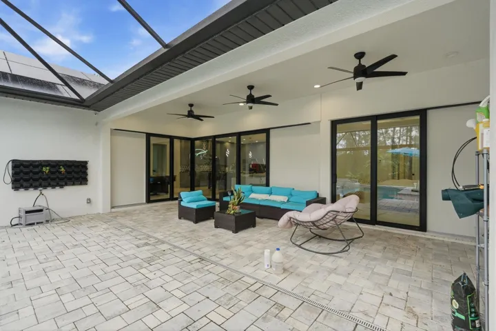 Expansive paver patio with a screened enclosure, multiple ceiling fans, and sliding glass doors