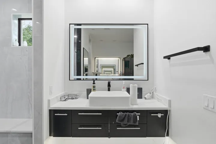 Illuminated mirror over a modern vanity with a vessel sink, dark cabinetry, and a light-toned countertop