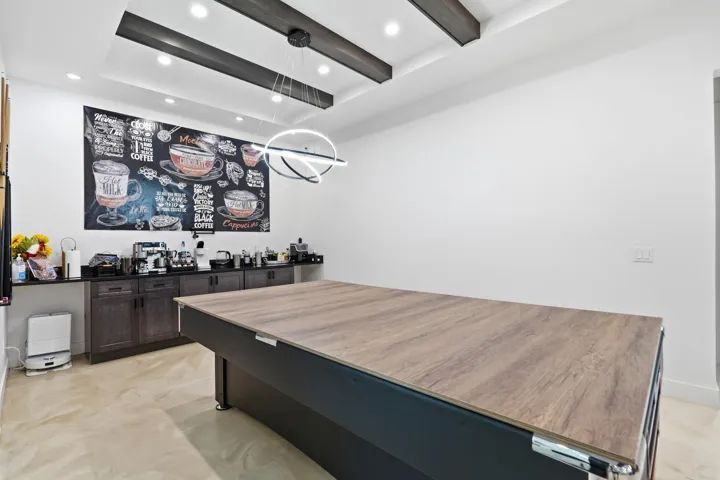 Recessed lighting, wood-finish ceiling beams, and a contemporary chandelier illuminate the space